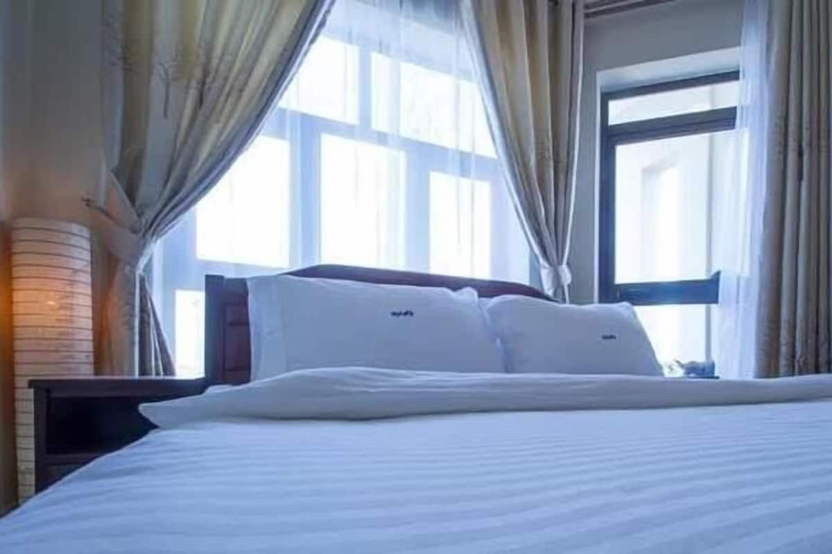 A hotel room with a large bed, curtains, and a window with blinds.