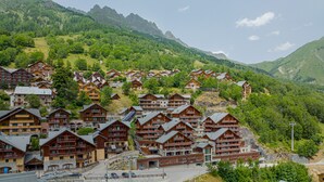 Un ensemble de bâtiments de style chalet en bois, dotés de balcons, se dressant sur un fond de collines et de montagnes verdoyantes.