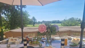 Area pranzo all'aperto con tavolo apparecchiato, circondato da sedie in vimini e riparato da un grande ombrellone.
