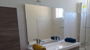 Un bagno con un lavandino bianco, uno specchio, un asciugamano e una doccia.