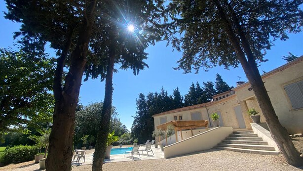 Area piscina con gradini che scendono in acqua, circondata da alberi e un edificio con tetto in tegole.