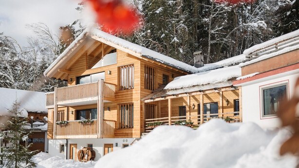 Eine Holzhütte mit Balkon, umgeben von schneebedeckten Bäumen.