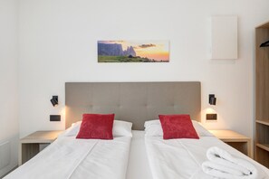 Een hotelkamer met twee bedden, een hoofdbord, nachtkastjes, een aan de muur hangend schilderij en een garderobe.