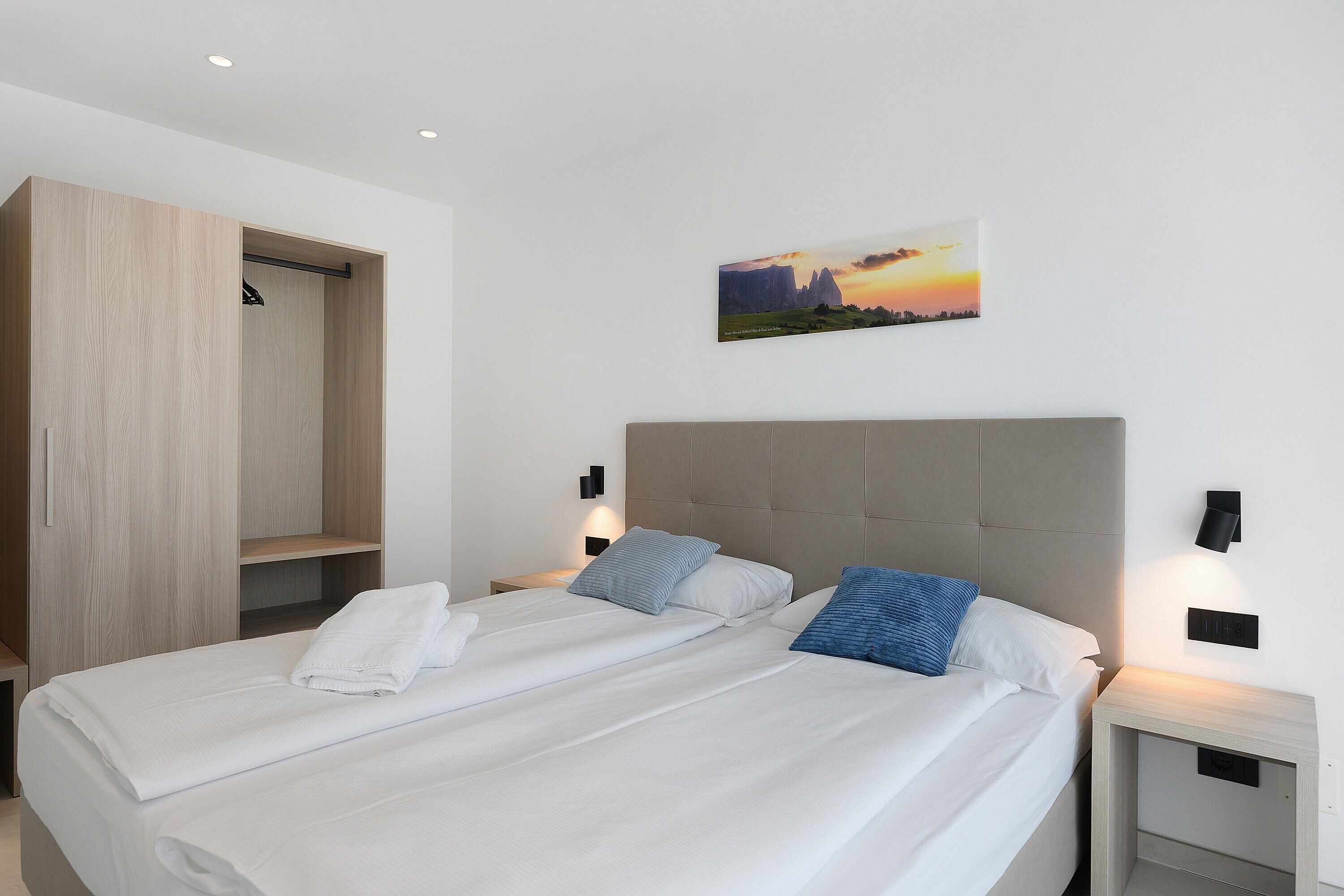 Een slaapkamer met een bed, twee nachtkastjes, een kledingkast en een aan de muur hangend schilderij.