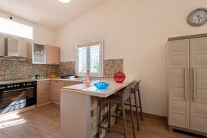 Une cuisine compacte dotée d’un four encastré, d’une fenêtre avec stores, d’un évier et d’un réfrigérateur.