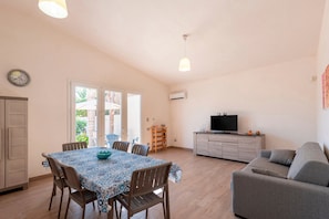 A dining area with a table and chairs, a sofa, a television, and a clock on the wall.