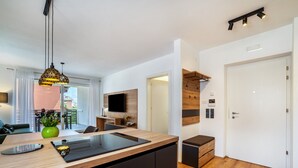 A modern kitchen with a wooden countertop, black cabinets, and a built-in stove. There is a dining area with a table and chairs, a green vase with flowers, and a hanging pendant light.