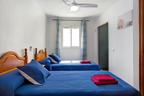 A room with two beds, a ceiling fan, a window with curtains, and a door.