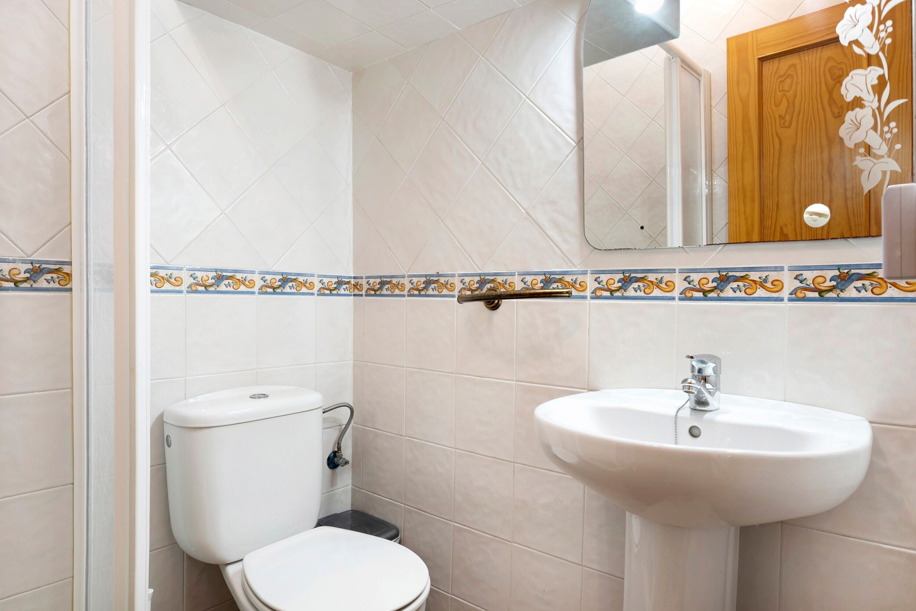 A bathroom with a toilet, sink, and a wooden door with a floral design.
