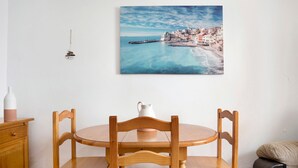 Un'area pranzo con tavolo e sedie in legno, un boccale bianco e un quadro raffigurante un borgo costiero.