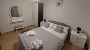Un dormitorio ordenado con cama, mesitas de noche, armario, espejo y una obra de arte en la pared.