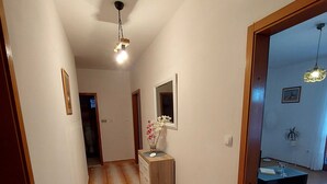 Un pasillo con piso de madera, un pequeño armario de madera con un jarrón de flores y un espejo en la pared.