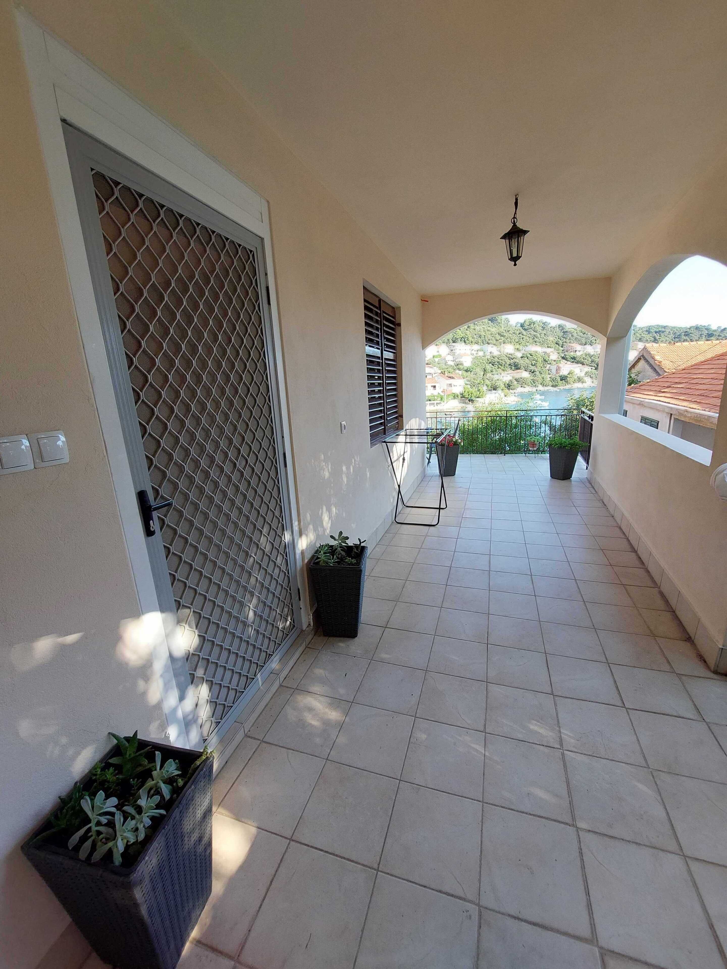 A covered balcony with tiled flooring, a metal gate, and potted plants.