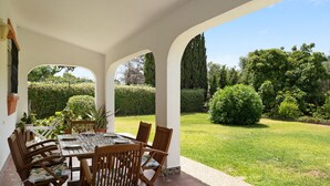 Eine überdachte Terrasse mit Esstisch, umgeben von Stühlen und Blick auf einen gepflegten Garten.
