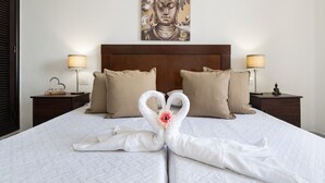 Een bed met een witte deken, twee kussens en een decoratieve zwaan met een bloem.