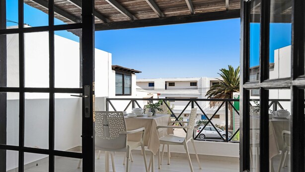 Een balkon met een tafel en stoelen, uitzicht op gebouwen en een palmboom.
