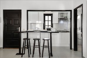 A kitchen with a black door, white cabinets, a countertop, and three stools.