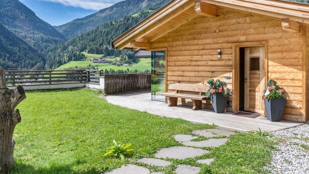A wooden cabin with a deck, a bench, and potted plants.