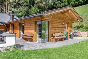 A wooden cabin with a deck, outdoor seating, and a glass door entrance.