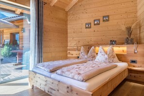 A wooden cabin bedroom with a bed, pillows, a nightstand, and a wall-mounted light fixture.