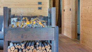 A fireplace with logs and burning embers, a wooden wall, and a visible electrical outlet.