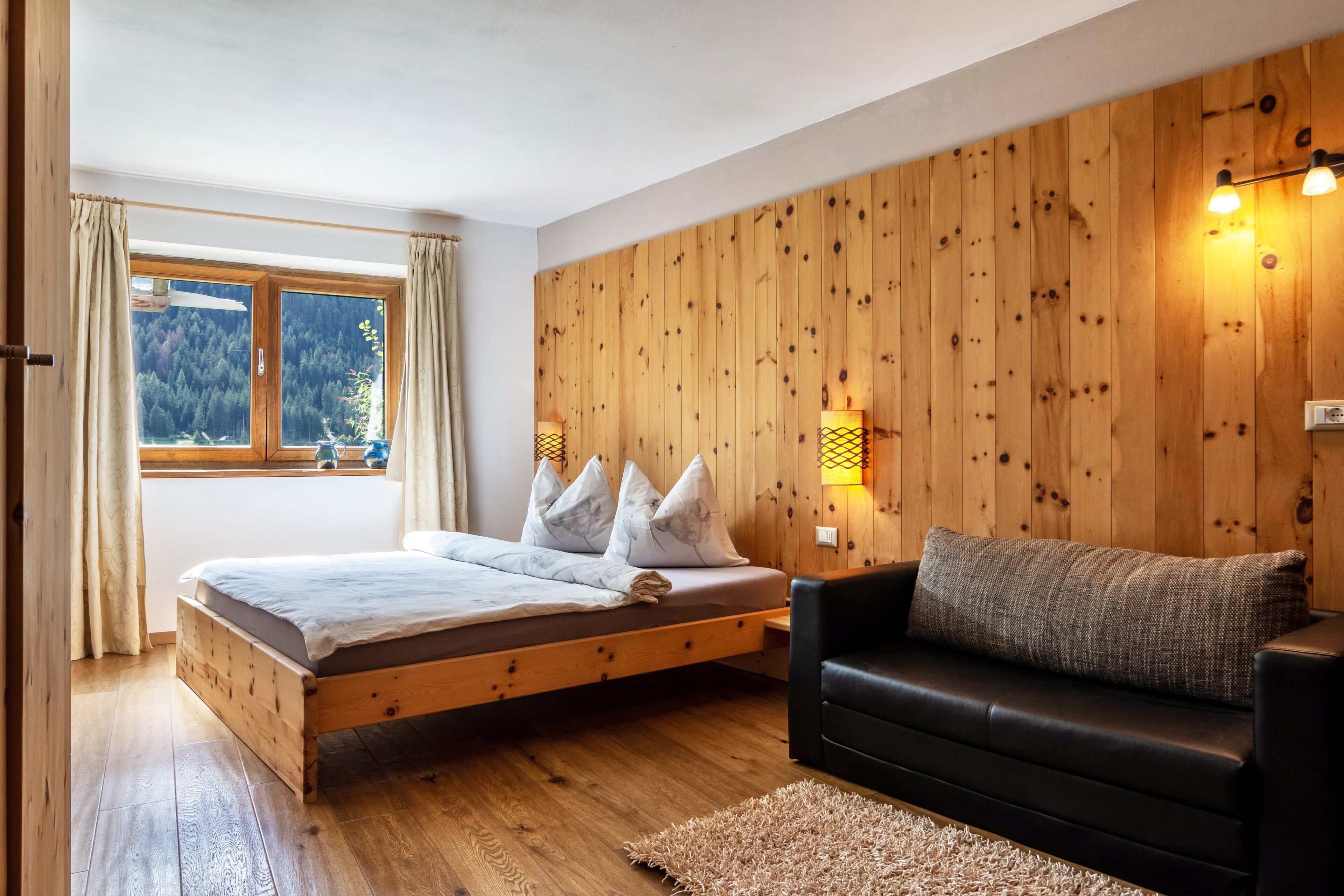 Un dormitorio con una cama de madera, un sofá negro, una ventana con cortinas y una pared de madera con luces de pared.
