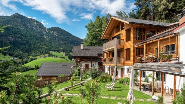 Een houten chalet met balkon, omgeven door een verzorgde tuin en een bergachtige achtergrond.