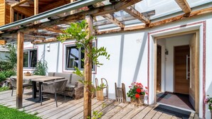 Een houten terras met een tafel en stoelen, een houten pergola en een deur met het nummer '190' op de muur.