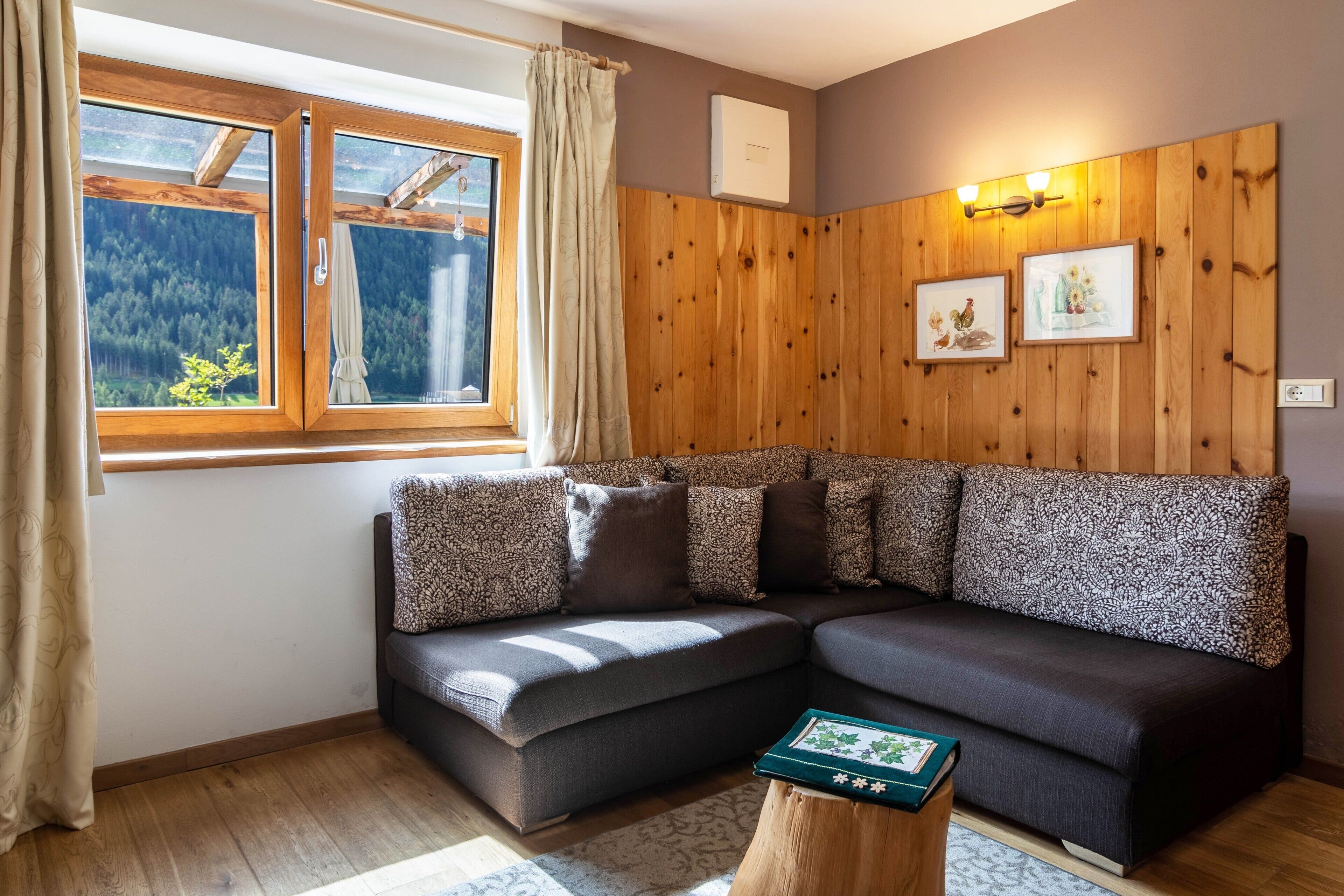 A modern living room with a sectional sofa, wooden panel walls, a window with curtains, and a small table with a book.
