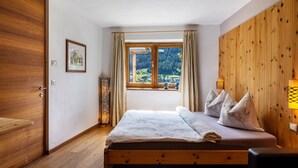 Een slaapkamer met een houten bed, een raam met uitzicht op een bos, en een houten wandpaneel.