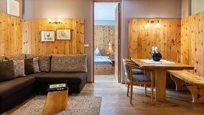 Een kamer met een houten wand, een bank, een eettafel met stoelen en een bed op de achtergrond.