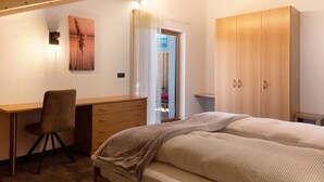 A bedroom with a wooden desk, a chair, a bed with two pillows, a wardrobe, and a painting on the wall. - Holiday Apartment 'Living Lerchna - Beautiful View' with Mountain View, Balconies and Wi-Fi (Maranza)