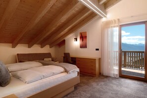 A bedroom with a bed, a desk, and a view of the mountains through a balcony.