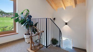 A staircase with a wooden handrail, a potted plant, and a view of a green landscape through a window. - Holiday Apartment 'Living Lerchna - Beautiful View' with Mountain View, Balconies and Wi-Fi (Maranza)