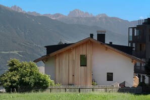 Uma cabana de madeira com telhado inclinado, uma pequena janela e uma chaminé, com montanhas ao fundo.