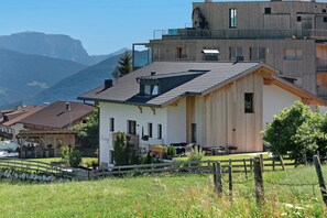 A modern building with a sloped roof, a wooden facade, and a view of mountains in the background.