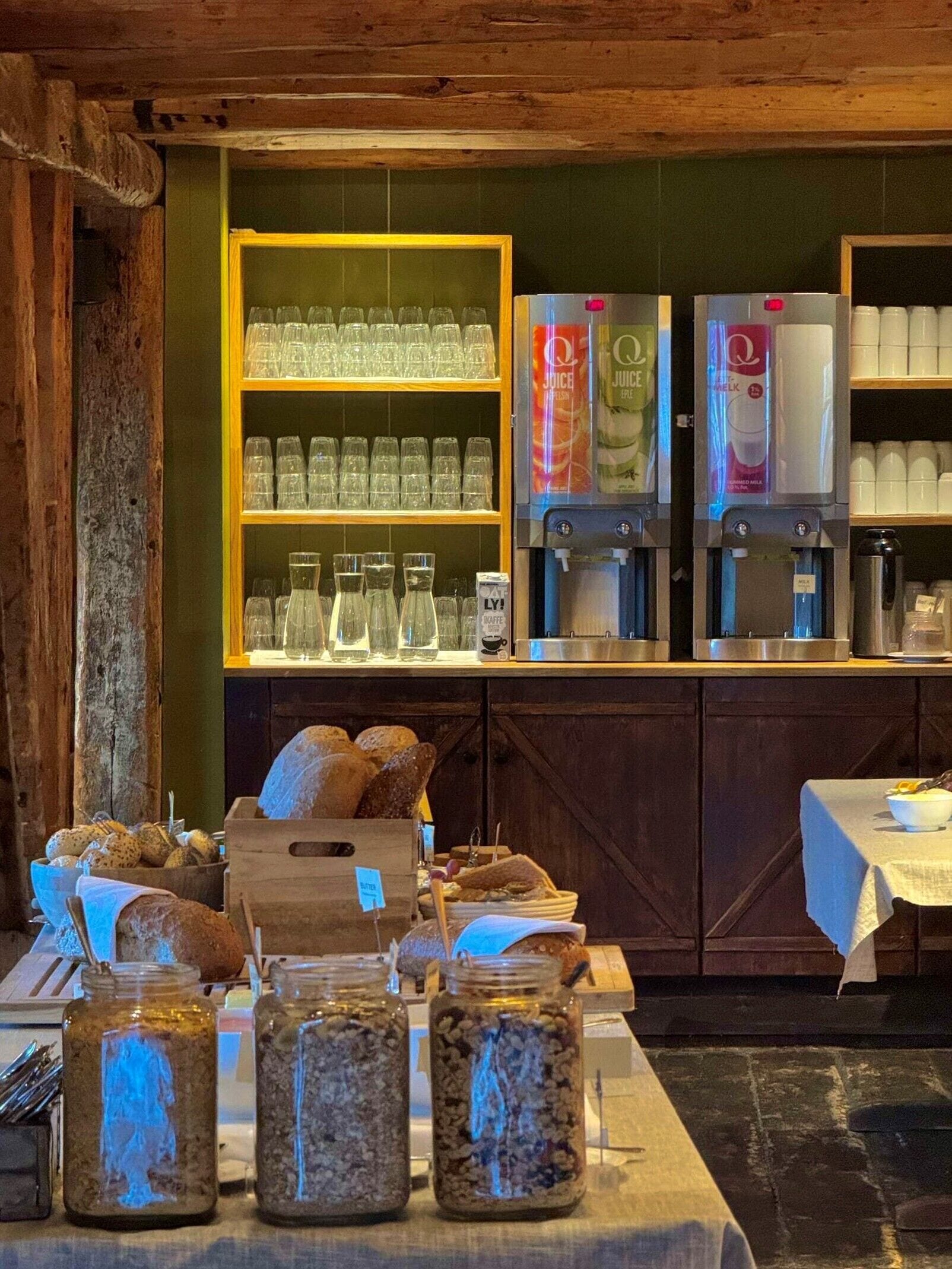 A rustic café with shelves of glasses, a coffee machine, and jars of food.