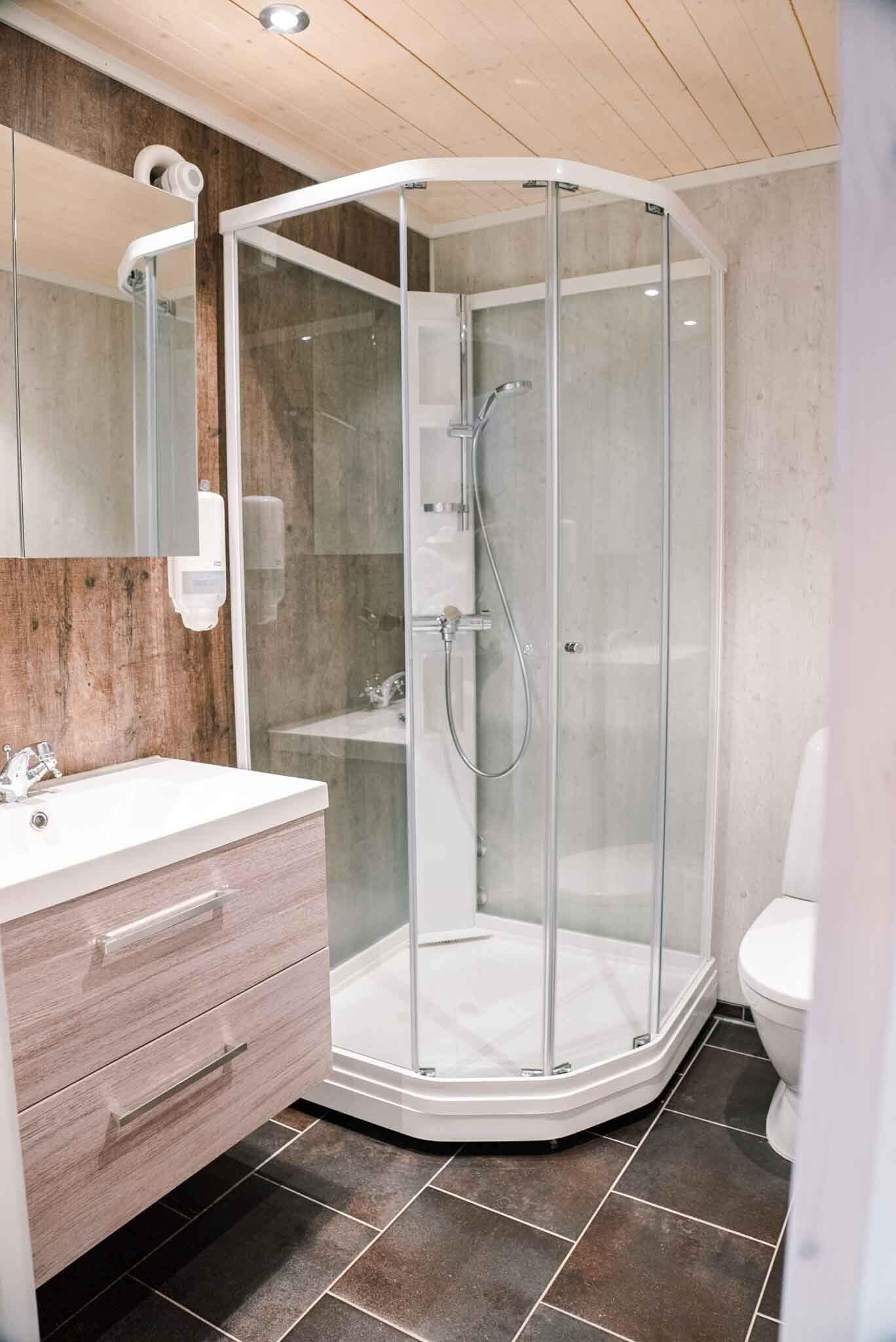 A modern bathroom with a glass-enclosed shower, a wooden vanity with drawers, and a white toilet.