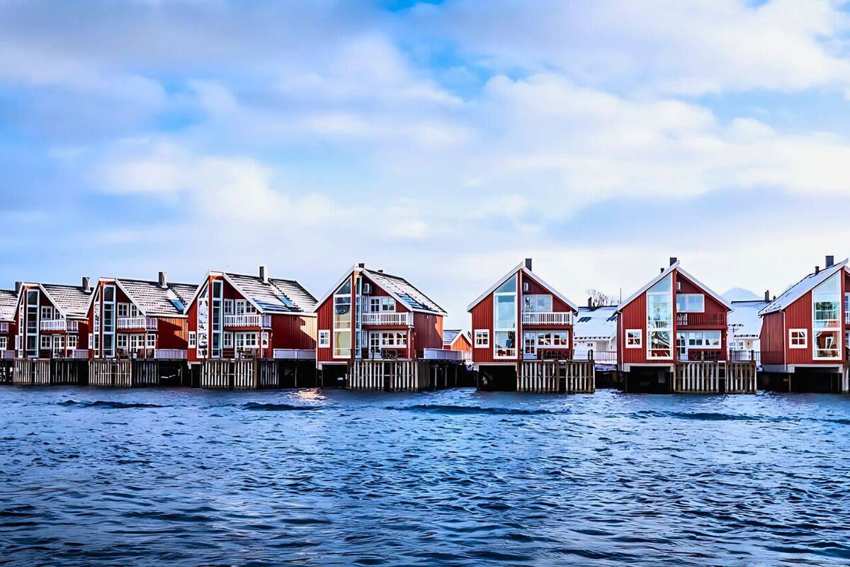 A row of red wooden houses with balconies, connected by wooden walkways over water.