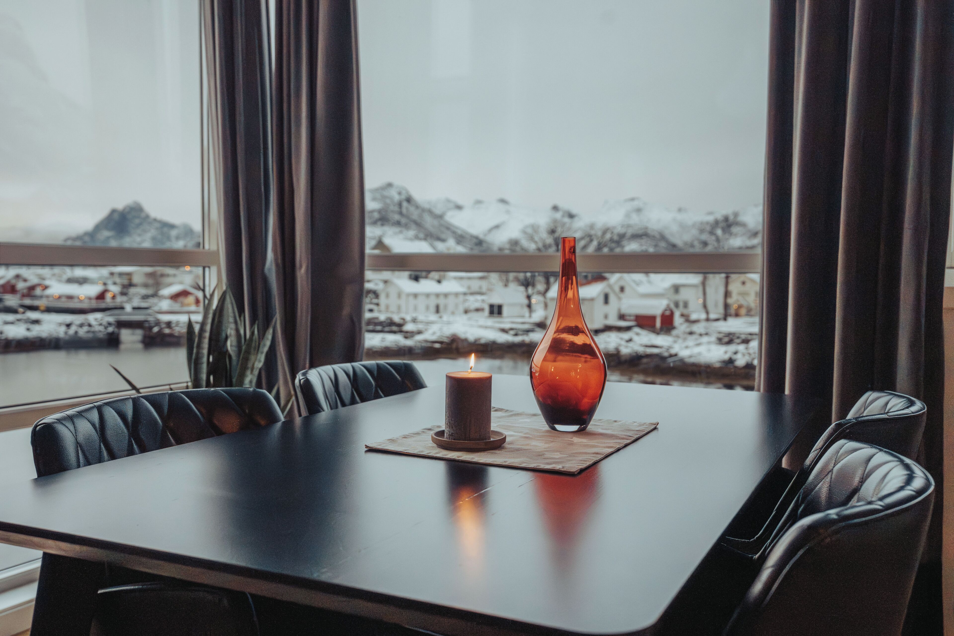 A dining table with a candle and a vase, set against a window with a snowy mountain view.