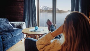 A room with a large window, a round wooden table, and a blue sofa. - Svinøya Rorbuer (Vagan)