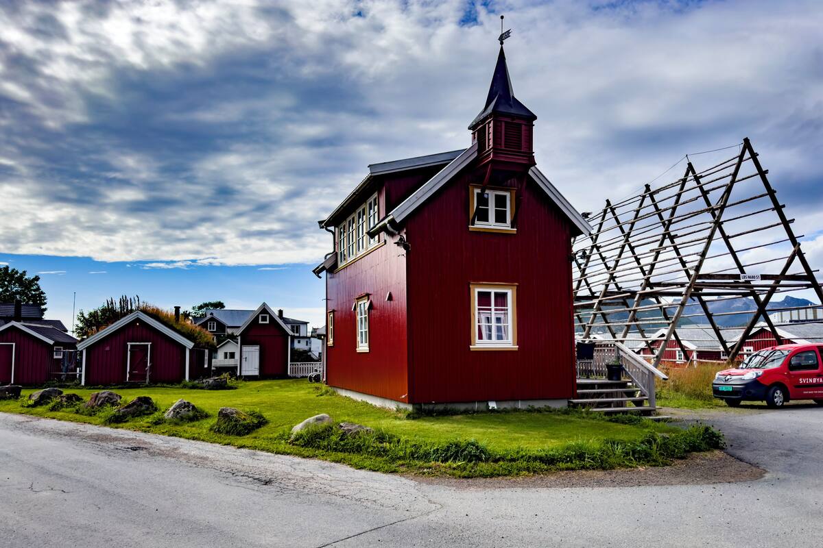 A red church with a steeple, a wooden staircase, and a red car parked nearby.