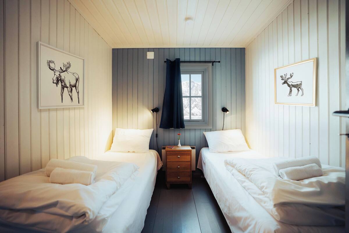 A room with two beds, a nightstand with a lamp, and framed pictures on the walls.