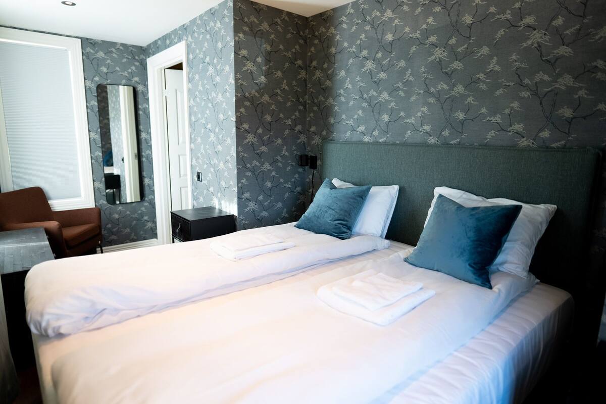 A hotel room with a large bed, two pillows, a nightstand, a chair, a desk, and a mirror.