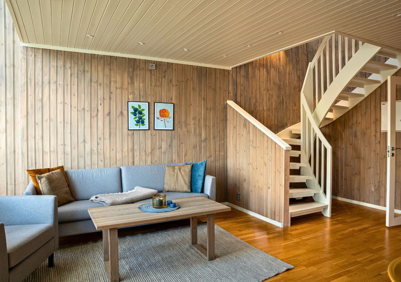 A modern living room with a wooden wall, a sofa, a coffee table, and a staircase.