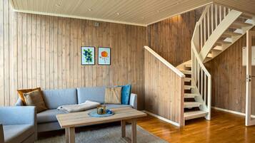 A modern living room with a wooden wall, a sofa, a coffee table, and a staircase.
