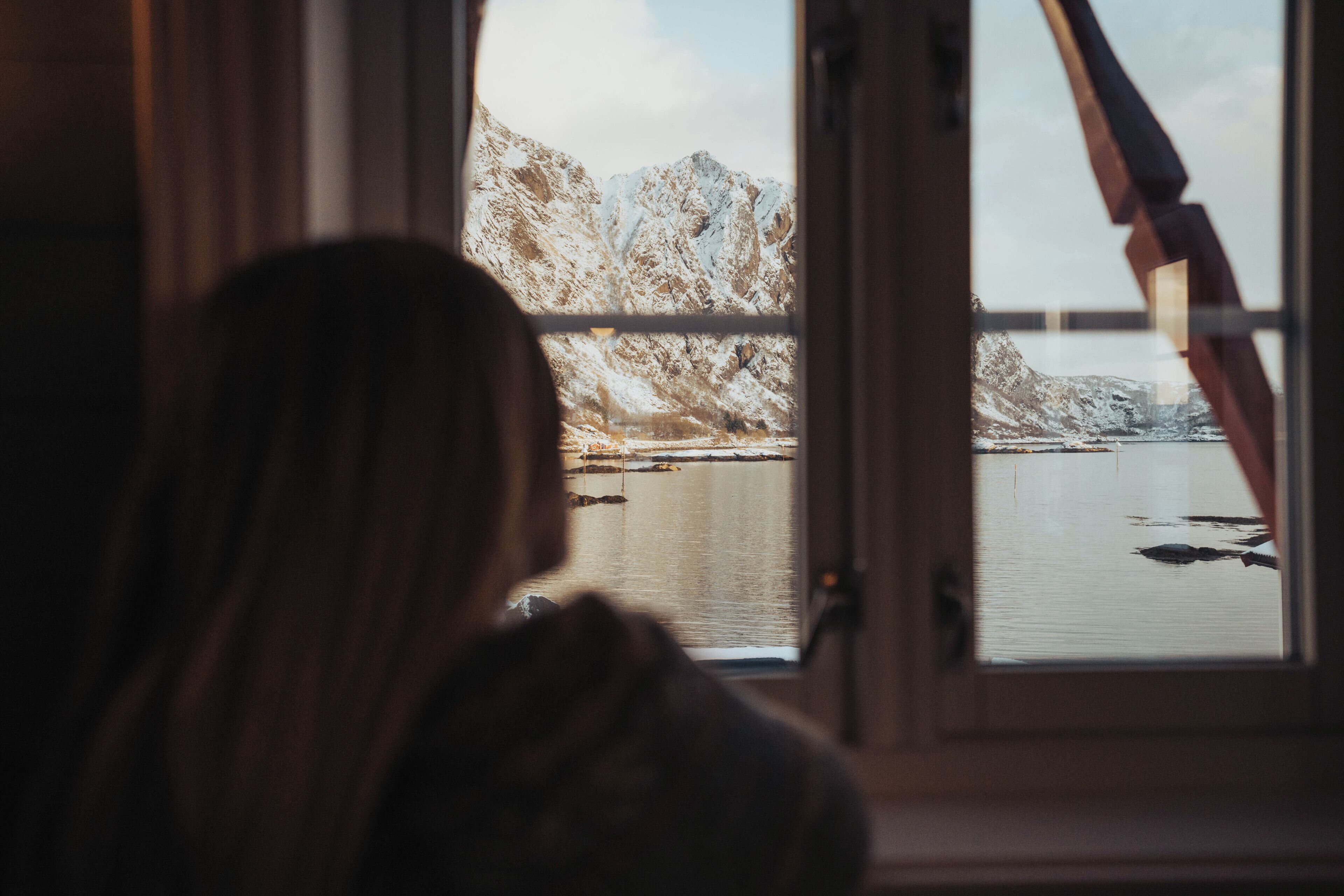 A person looking out of a window with a view of mountains and a body of water.