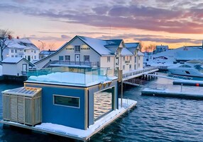 Una propiedad frente al agua con un nivel superior envuelto en vidrio, un muelle y un paisaje cubierto de nieve.