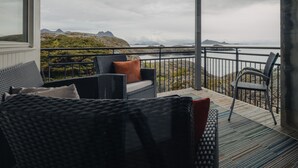 A balcony with wicker furniture, a view of rocky terrain and distant mountains, and a railing. - Svinøya Rorbuer (Vagan)