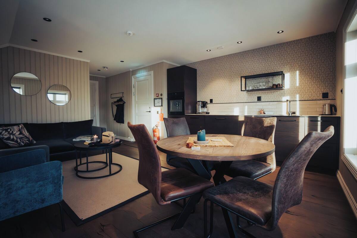 A modern living room with a round wooden table, dark leather chairs, and a blue sofa.